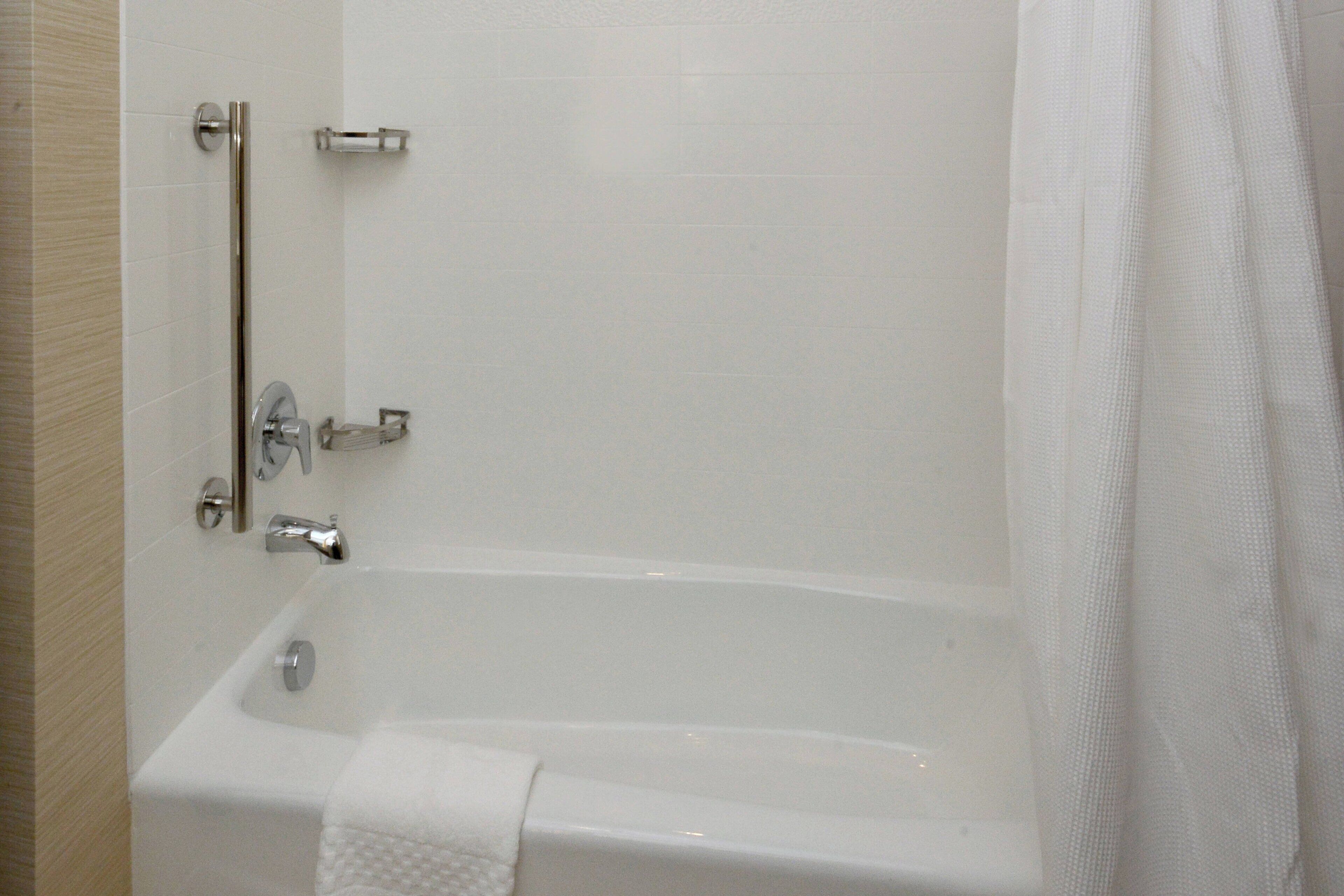 A white bathtub with a towel, a grab bar, and a shower curtain.