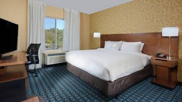 A hotel room with a large bed, a desk with a chair, a TV, and a window with curtains.