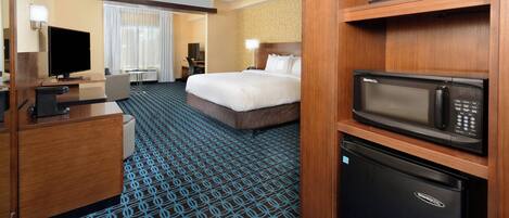 A hotel room with a bed, a desk with a computer, a microwave, and a refrigerator.