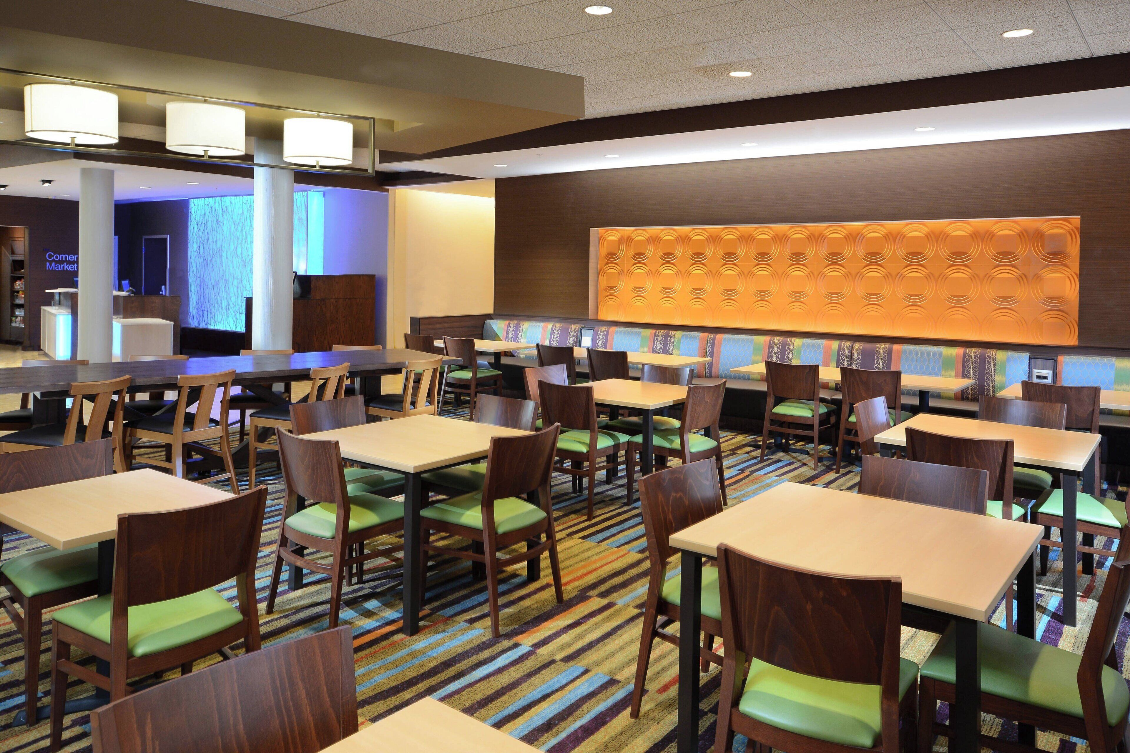 A hotel dining area with multiple tables and chairs, a patterned carpet, and a large wall with circular designs.