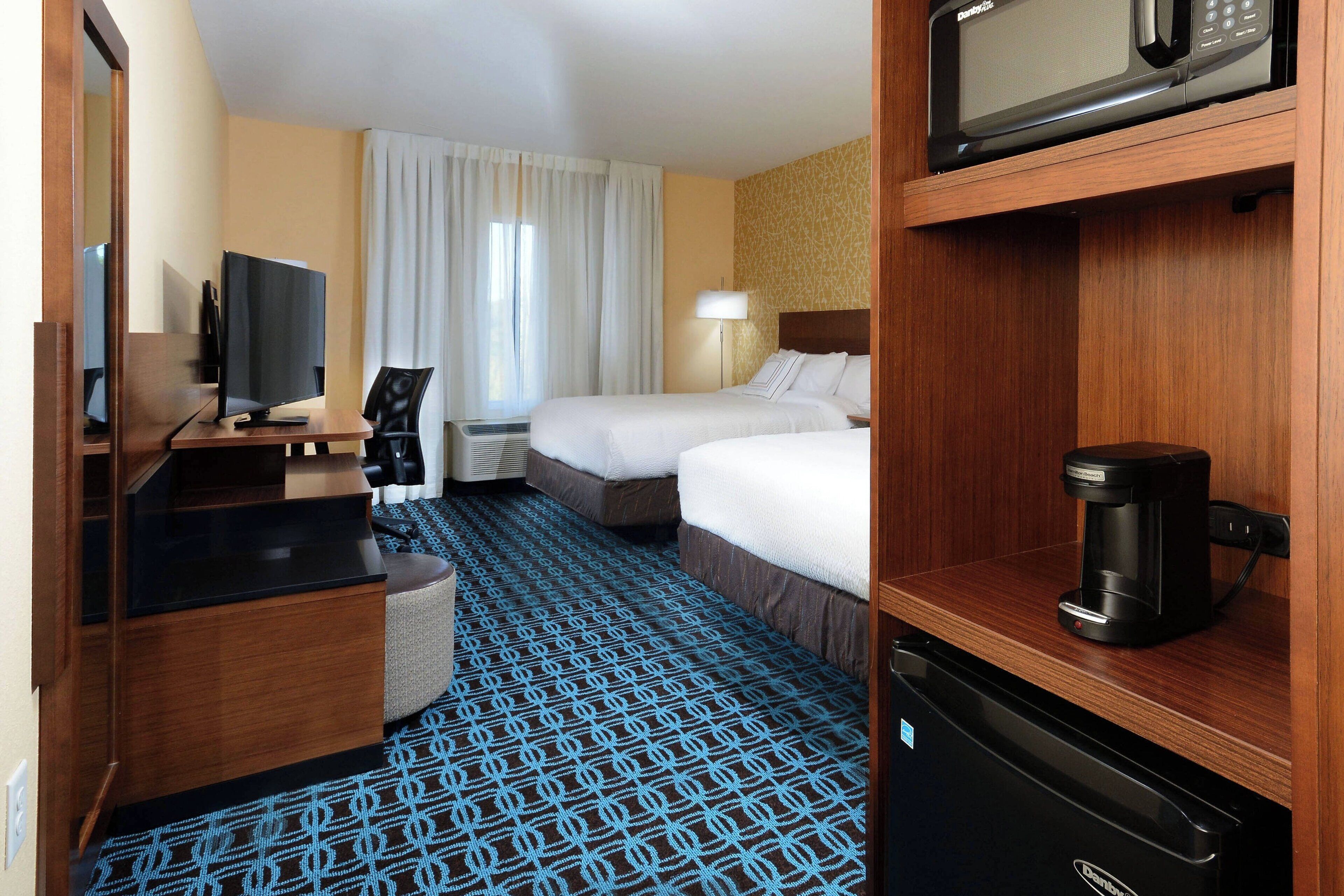 A hotel room with a bed, a desk with a computer, a microwave, and a coffee maker.