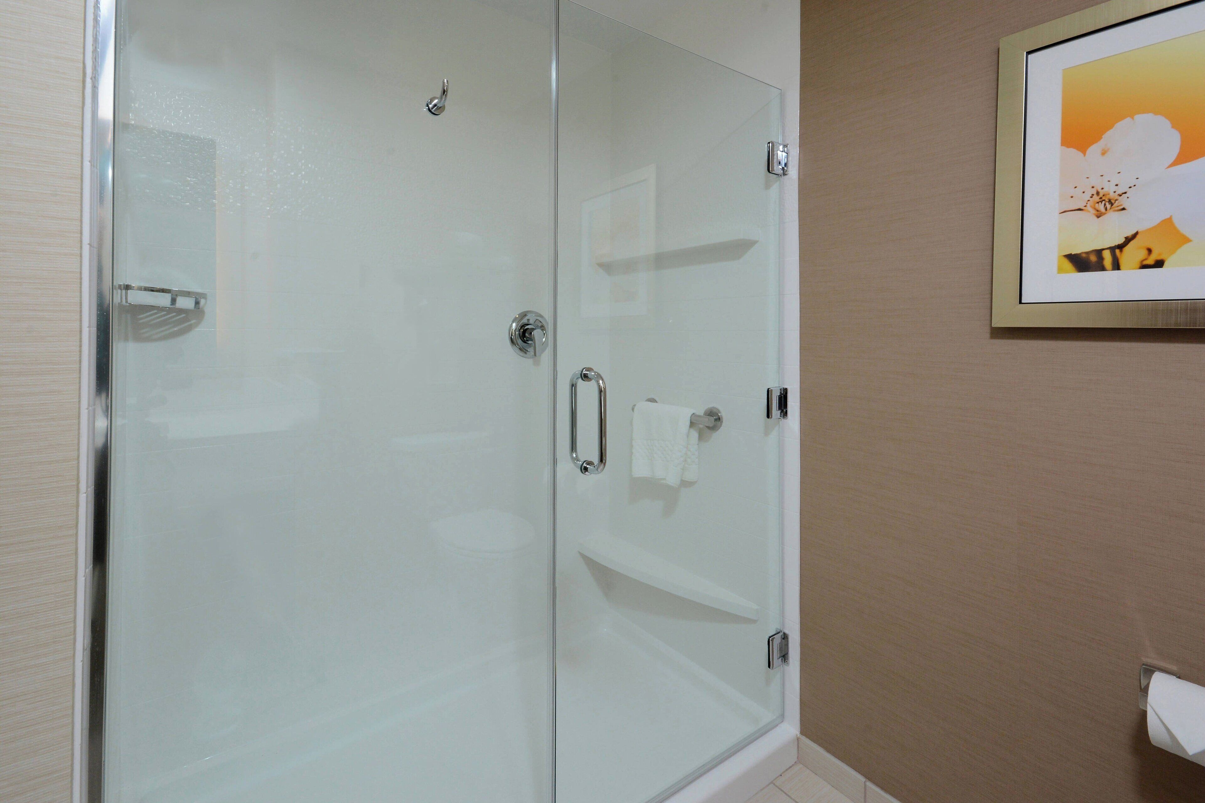 A glass-enclosed shower with a towel rack and a shelf.