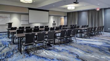 Un salón de conferencias con una pantalla grande, varias mesas y sillas dispuestas para reuniones.