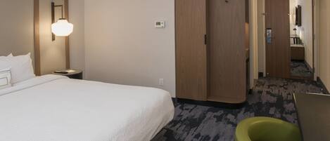 Une chambre d’hôtel avec un grand lit, un fauteuil vert, une armoire et une salle de bain visible à travers une porte ouverte.