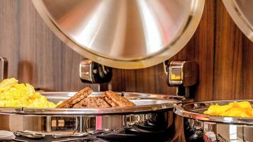 A buffet setup with various food items, including scrambled eggs and meat, on stainless steel trays.