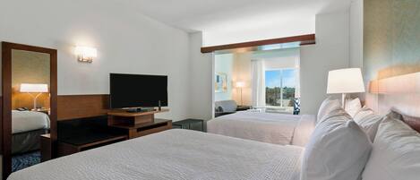 A hotel room with two beds, a flat-screen TV, bedside lamps, a desk, and a window with a view.