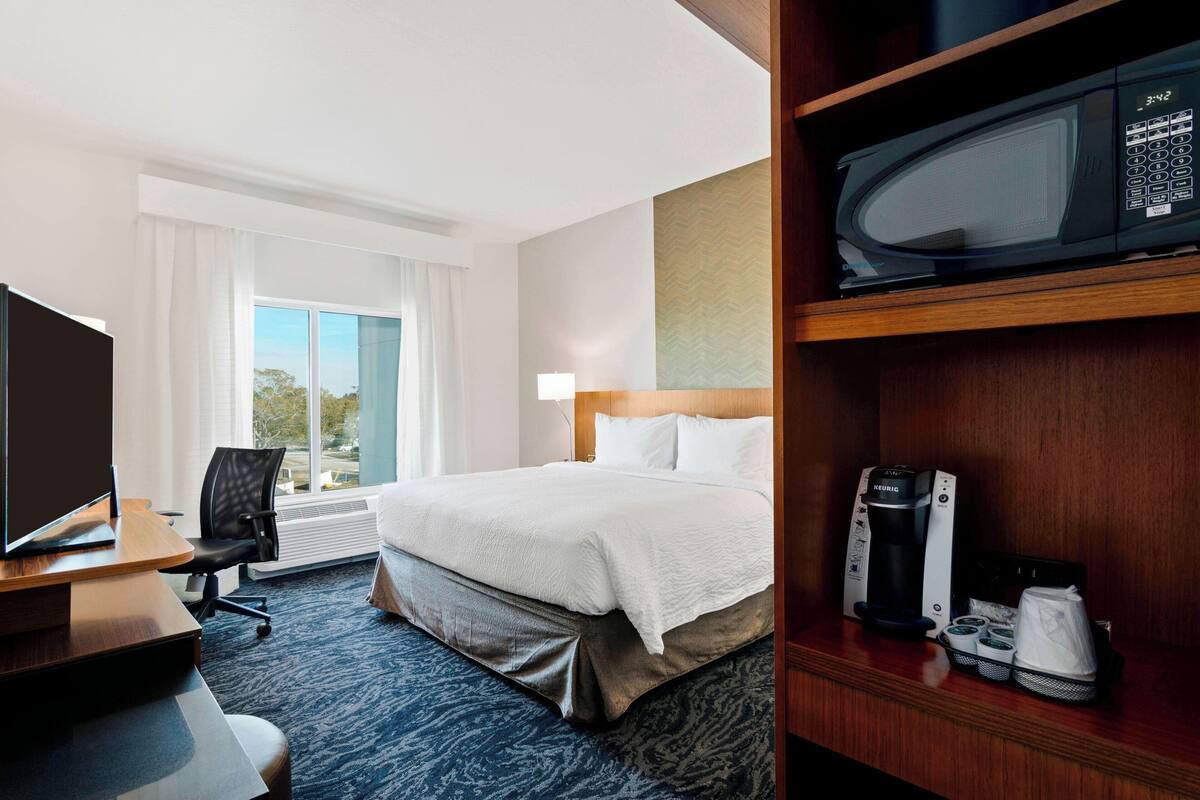 Habitación de hotel con cama, escritorio con computadora, microondas y cafetera.