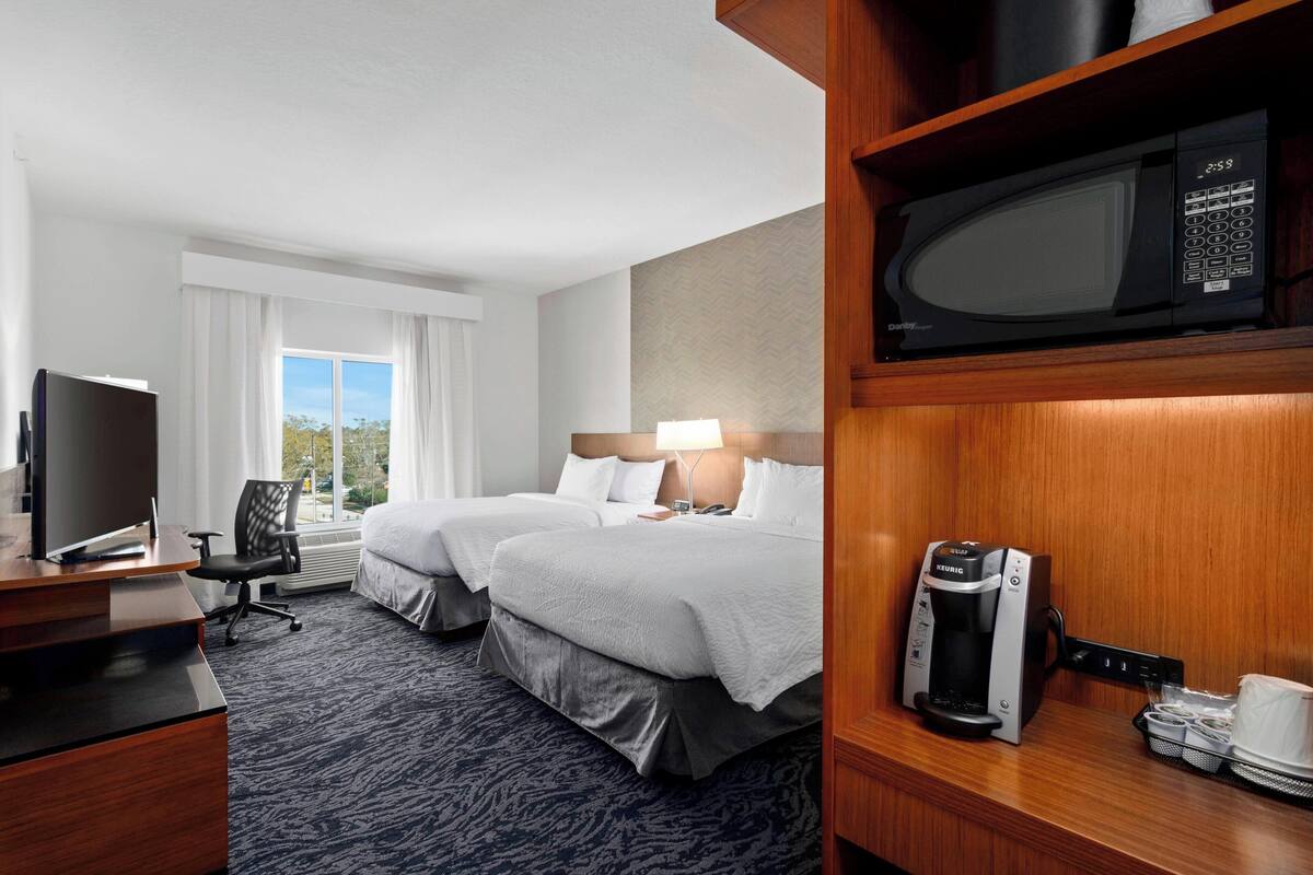 Habitación de hotel con cama, escritorio, computadora, televisor, microondas y cafetera.
