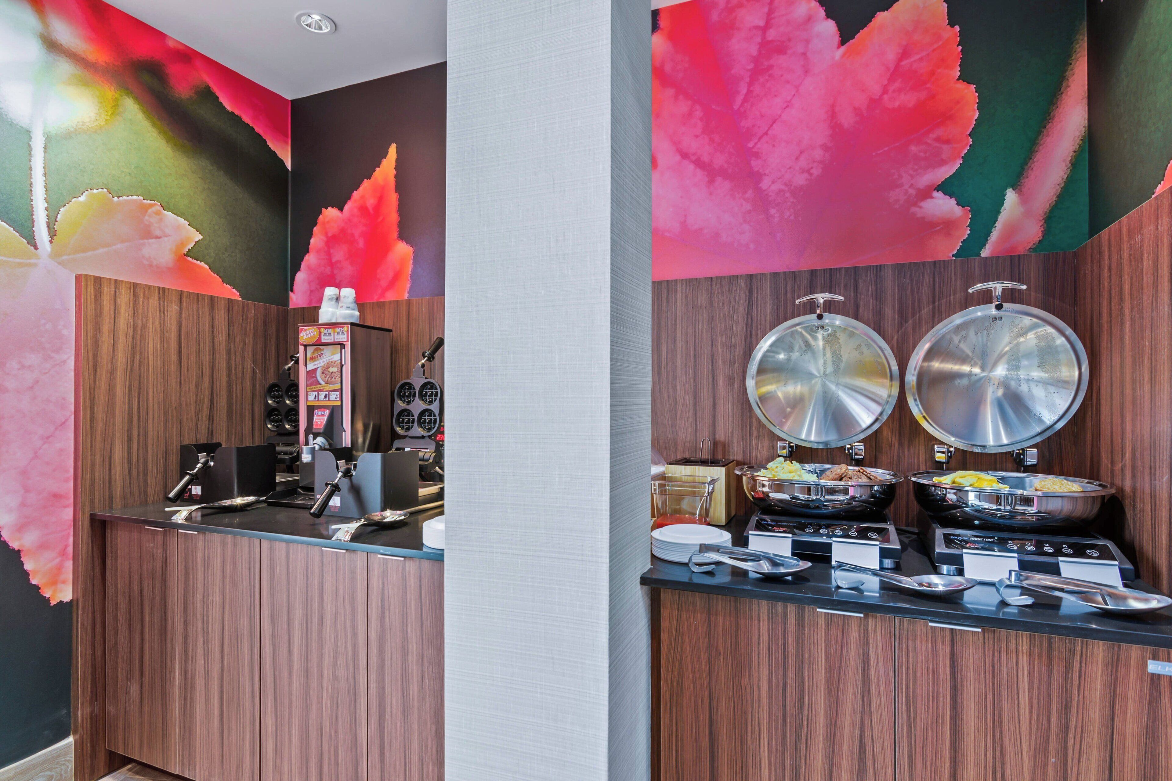 Zona de buffet con máquina de café, platos calientes y diversos alimentos.