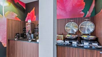 Zona de buffet con máquina de café, platos calientes y diversos alimentos.
