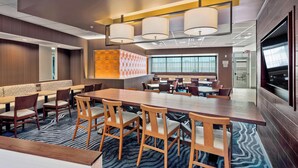 A modern hotel lobby with a large dining area, seating arrangements, and a television screen.