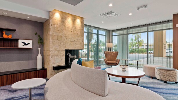 A modern hotel lobby with a stone fireplace, comfortable seating, and large windows offering a view of the outdoors.