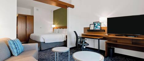 Una habitación de hotel con cama, sofá, televisor, escritorio y una pequeña mesa.