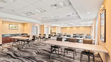 A conference room with multiple tables and chairs, carpeted flooring, and ceiling lights.