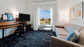 A hotel room with a desk, chair, sofa, and a large window with curtains.