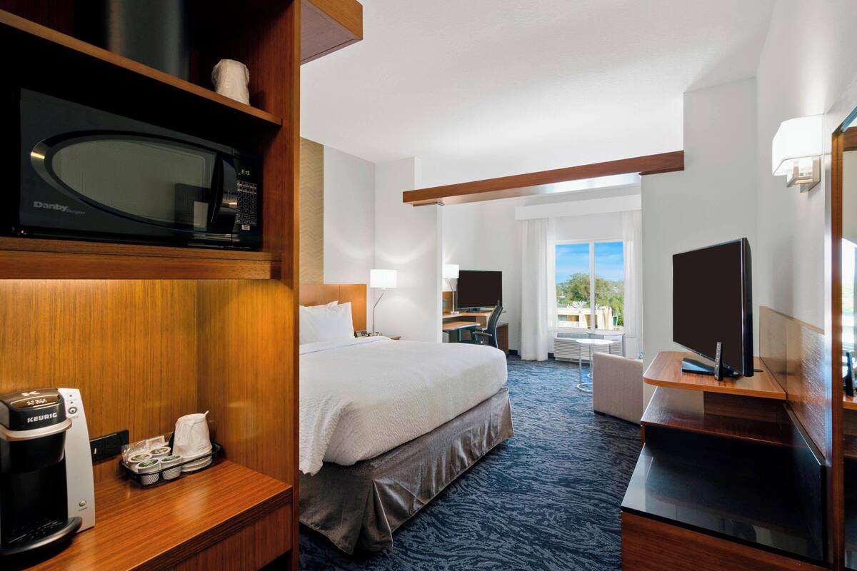 Habitación de hotel con cama, escritorio, televisor, cafetera y vista al exterior.