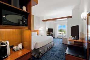 Habitación de hotel con cama, escritorio, televisor, cafetera y vista al exterior.