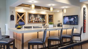 A modern bar area with a wooden counter, bar stools, and a variety of bottles and glasses.