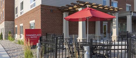 A fenced outdoor patio area with a red umbrella, outdoor seating, and a sign for Towneplace Suites Marriott.