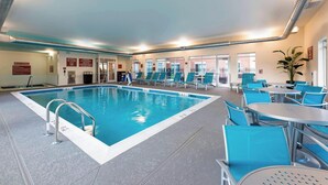 An indoor swimming pool with clear water, surrounded by blue chairs and tables, and a tiled floor.