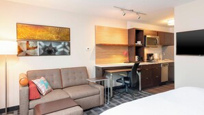 A modern hotel room with a sofa, a small desk, a microwave, and a TV.