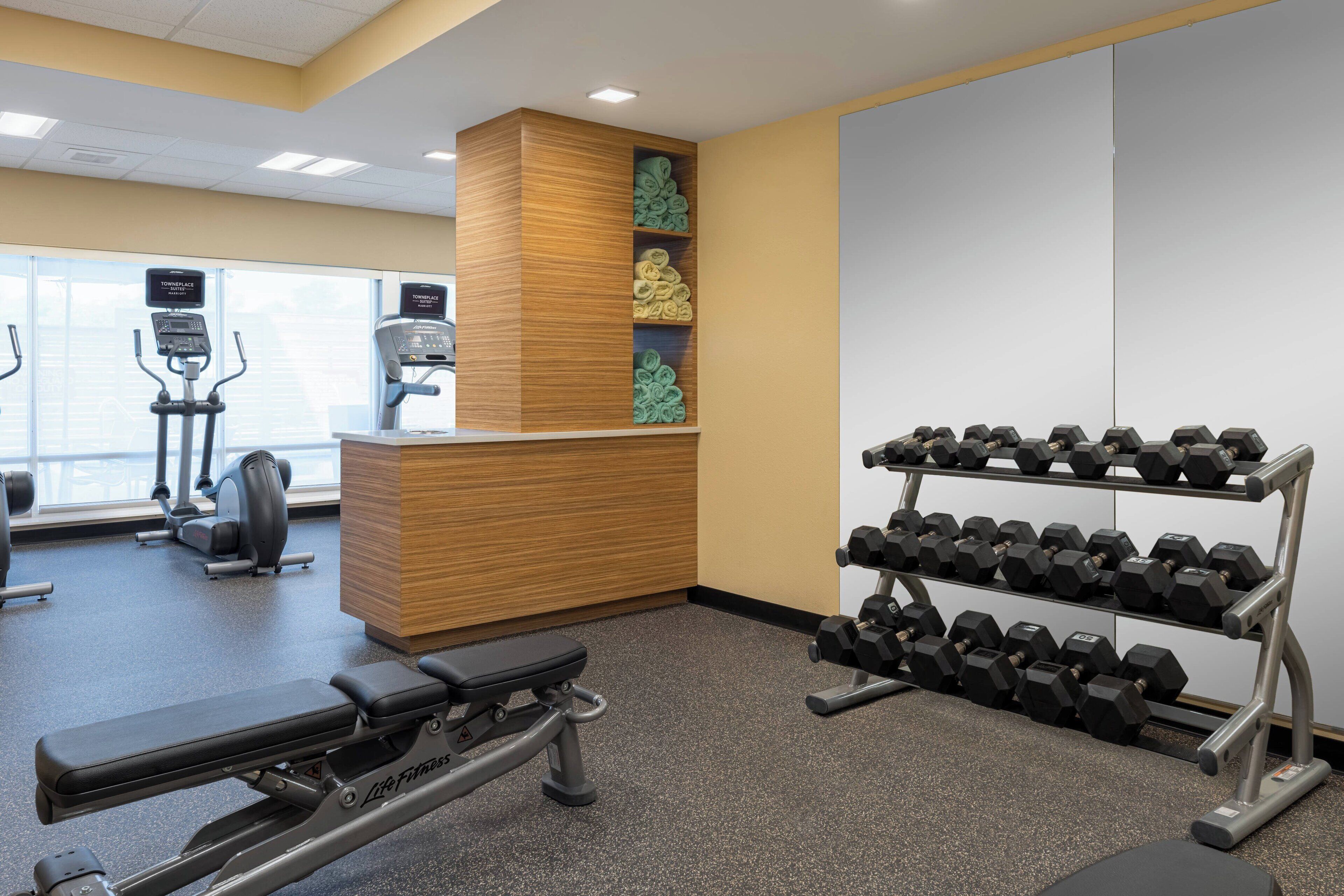 A gym with cardio machines, dumbbells, and a bench.