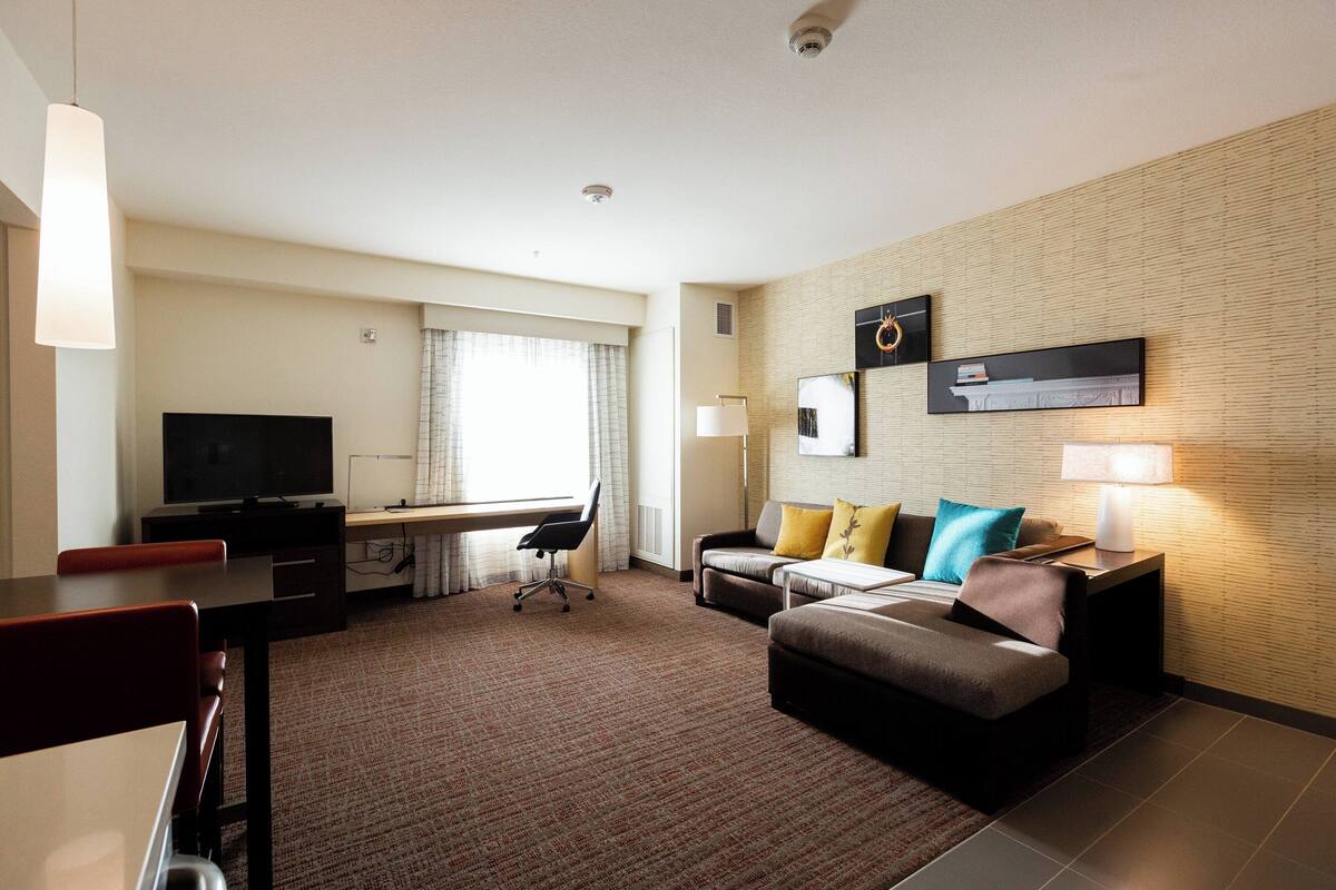 Una habitación de hotel con televisión de pantalla plana, un escritorio, un sofá y una lámpara.