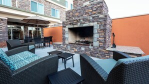 Un patio exterior con mobiliario de mimbre, una chimenea de piedra y un comedor con paredes de vidrio.