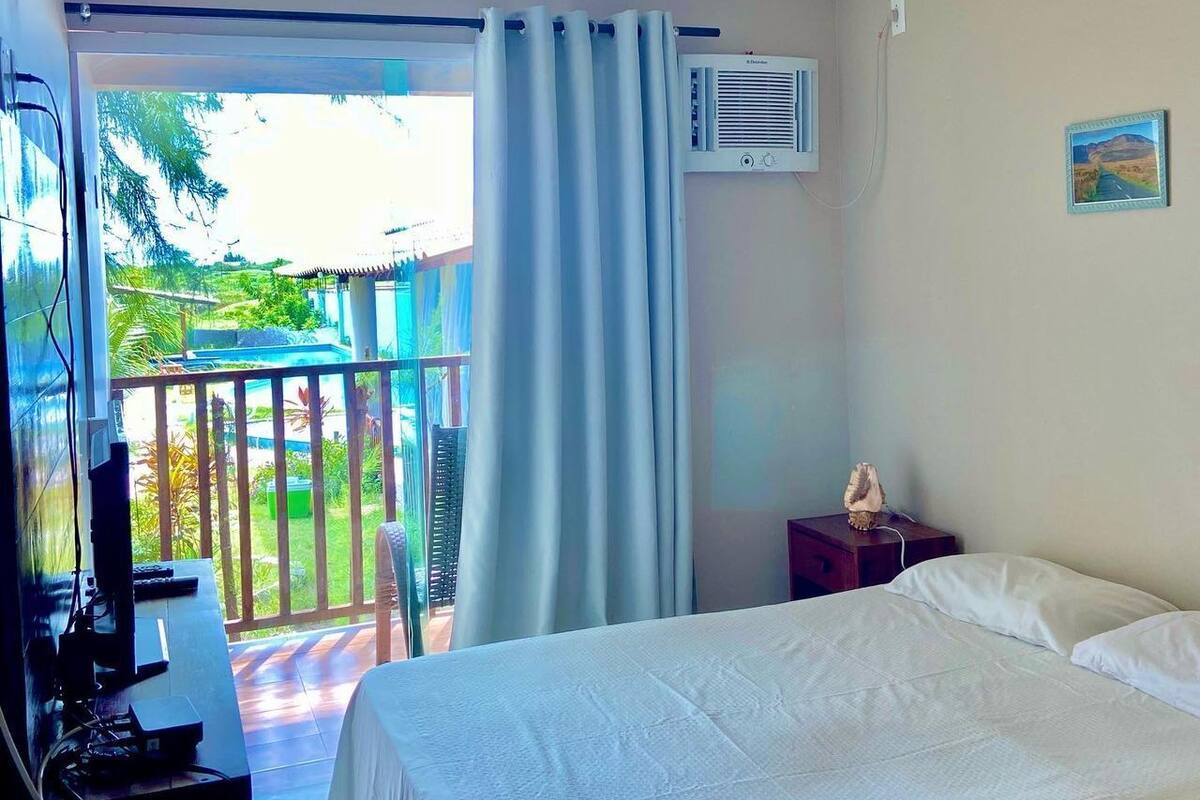 Une chambre d’hôtel comprenant un lit, un bureau avec un ordinateur, un appareil de climatisation et une vue sur un balcon doté d’une balustrade.