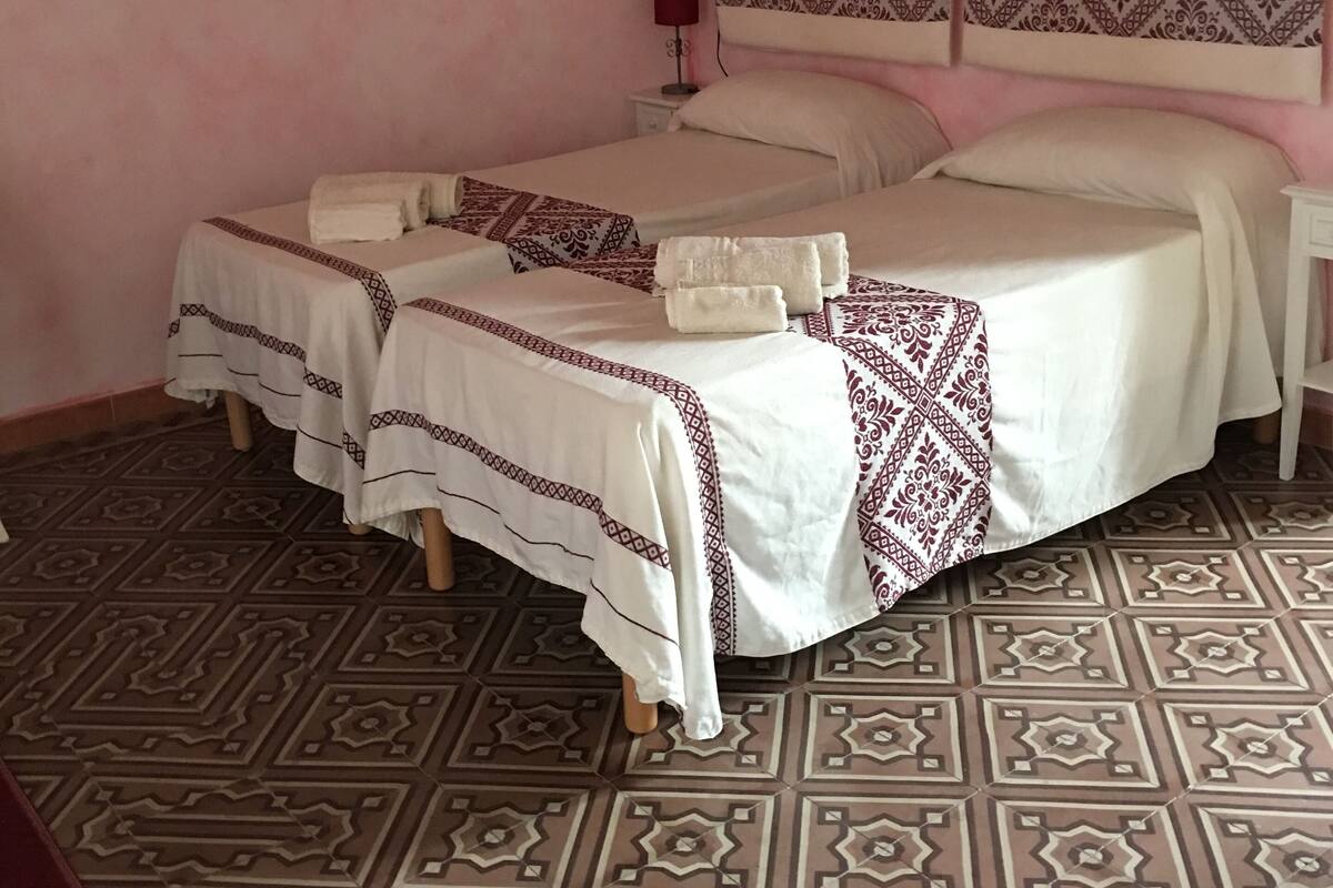 A room with two beds, patterned floor tiles, and a headboard with a geometric design.