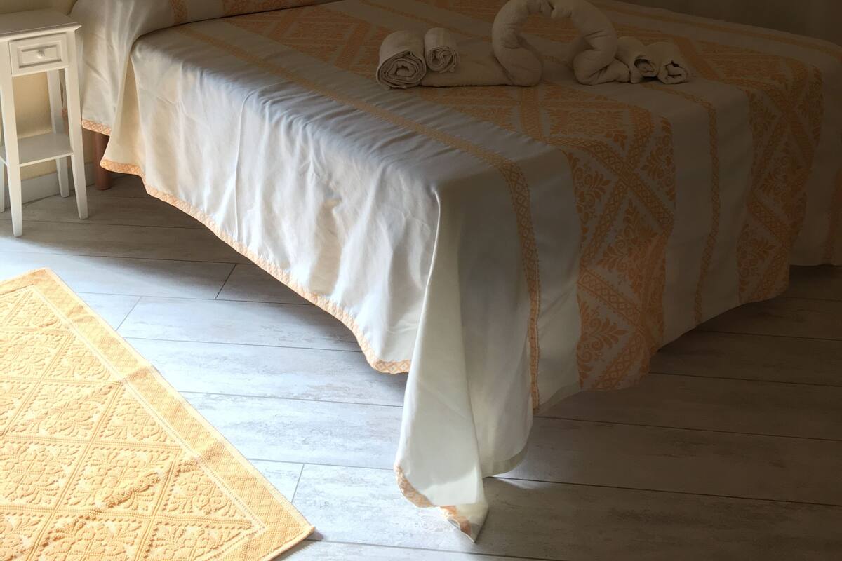 A neatly made bed with a patterned bedspread, a bedside table with a lamp, and a small rug on the floor.