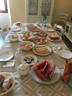 A dining table set with various dishes, including bread, pastries, and a watermelon. - Affittacamere Le Gemelle (Luras)