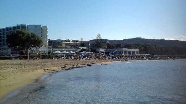 A beach with clear water, a sandy shore, and buildings in the background. - Hotel Anna Apartments (Gouves)