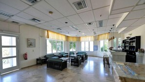 A spacious room with a large window, a fire extinguisher, and a kitchen area with a counter and stools. - Hotel Anna Apartments (Gouves)