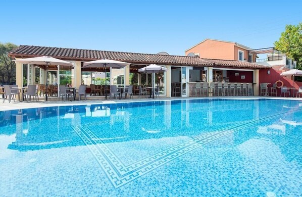 A swimming pool with a tiled deck, outdoor seating, and a covered patio area. - Eriva Apartments (Corfu)