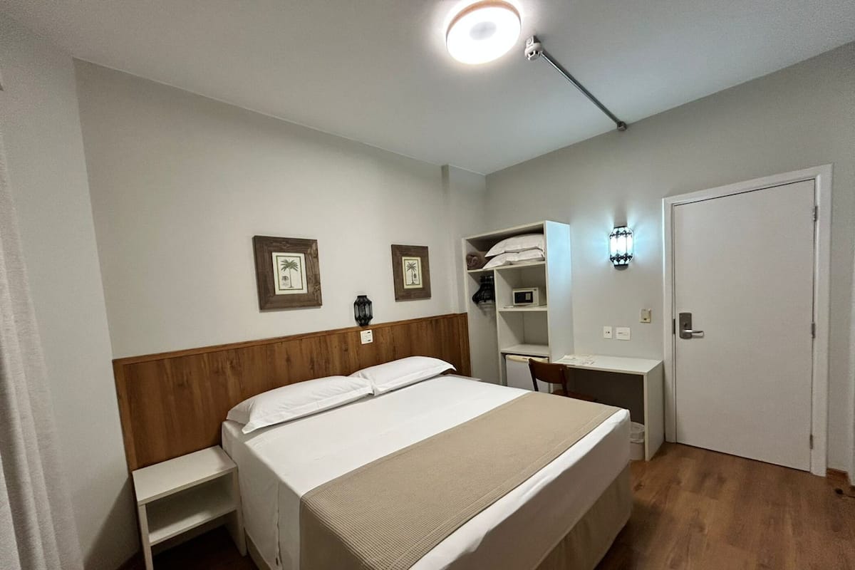 A bedroom with a bed, bedside table, wardrobe, desk, and a lamp.