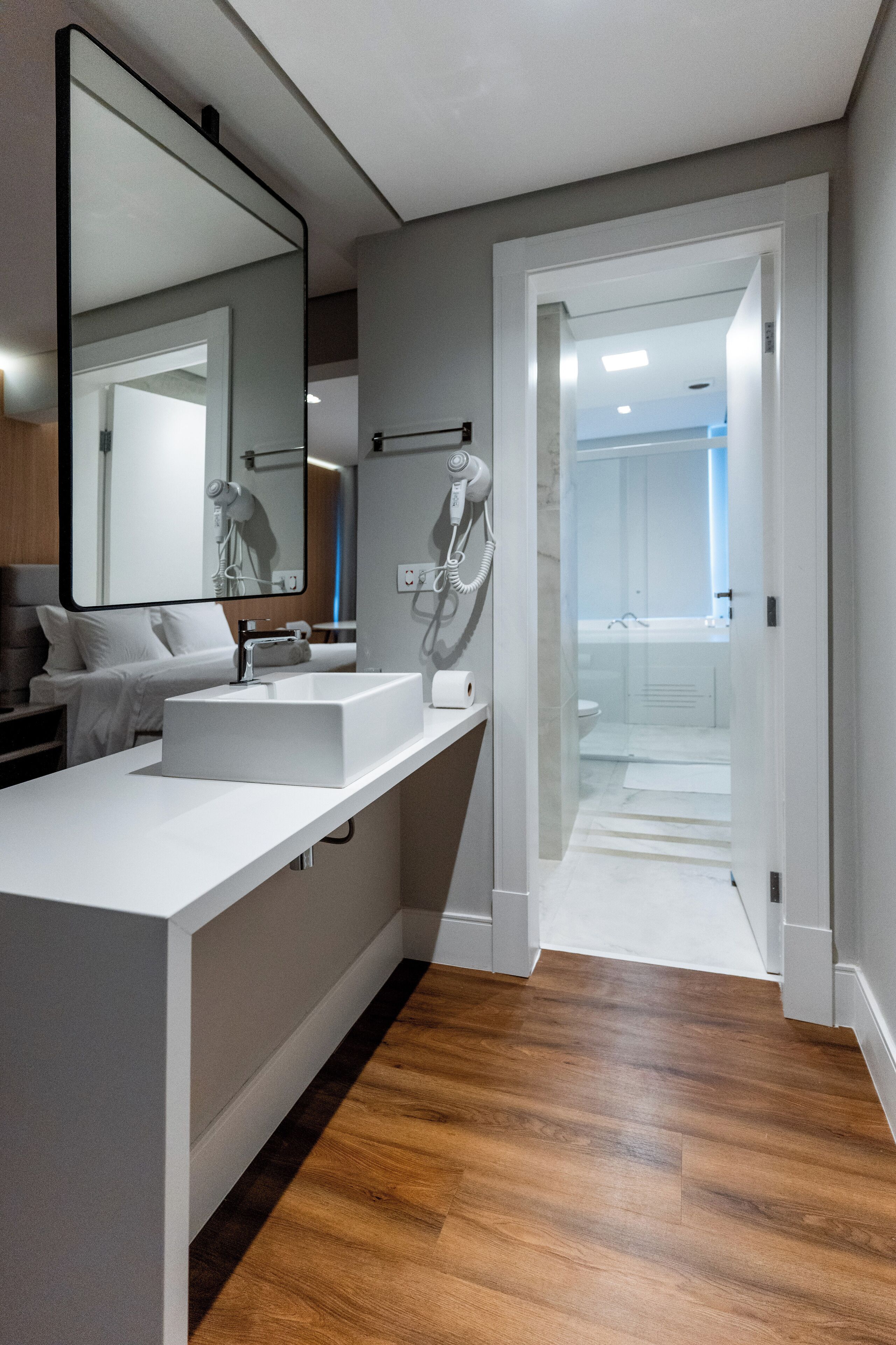 Uma casa de banho moderna com um espelho grande, uma sanita branca e um secador de cabelo na parede.