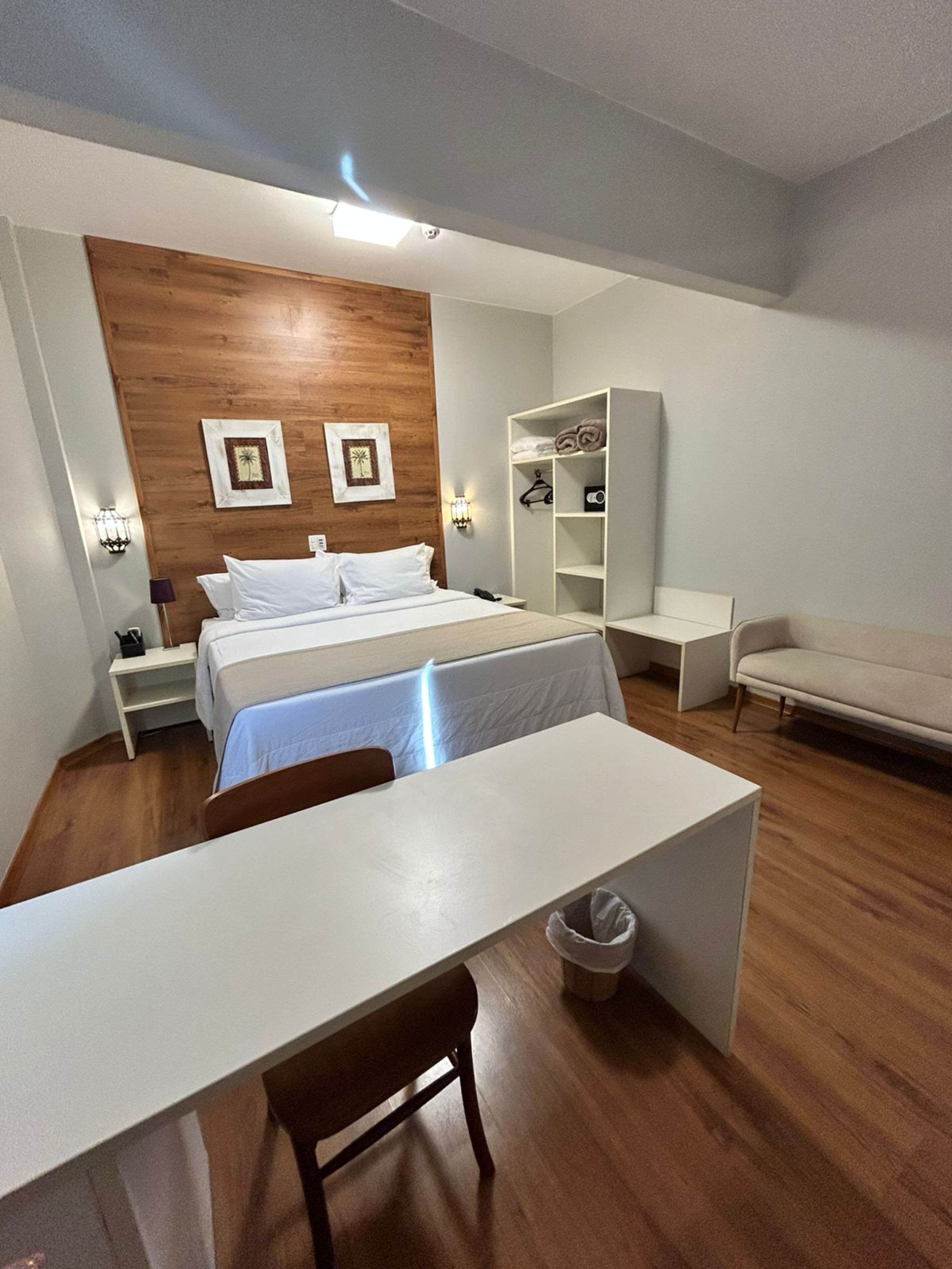 Habitación de hotel moderna con una pared de acento de madera, una cama con ropa blanca, un escritorio con una silla, un sofá y un armario.
