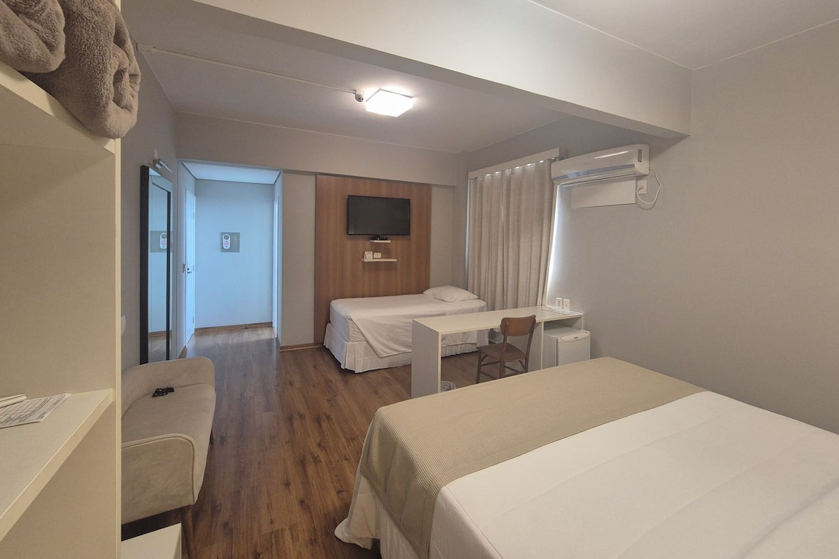 A hotel room with a bed, a desk, a chair, a television, and a bathroom visible through an open door.