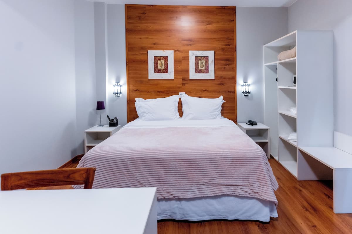 A modern bedroom with a wooden headboard, a bed with white and pink bedding, bedside tables with lamps, and a white wardrobe.