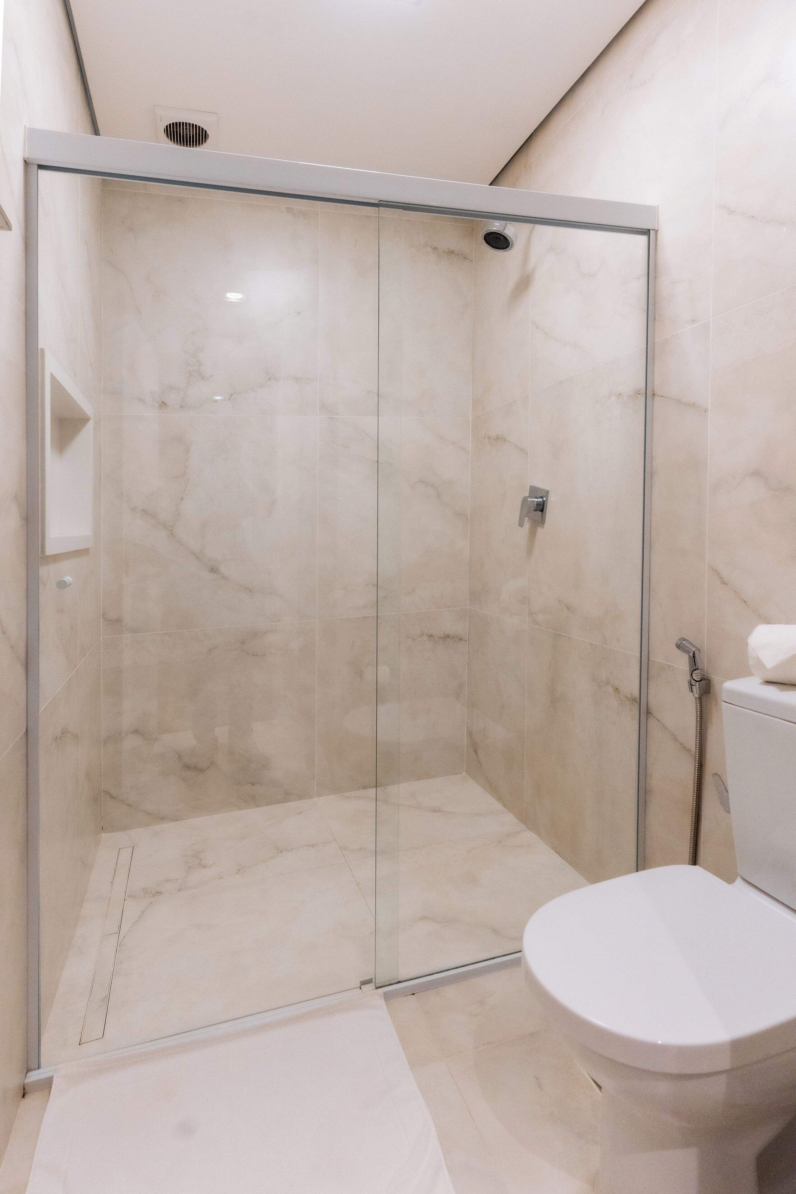 Un baño moderno con ducha acristalada, inodoro blanco y suelo de mármol.