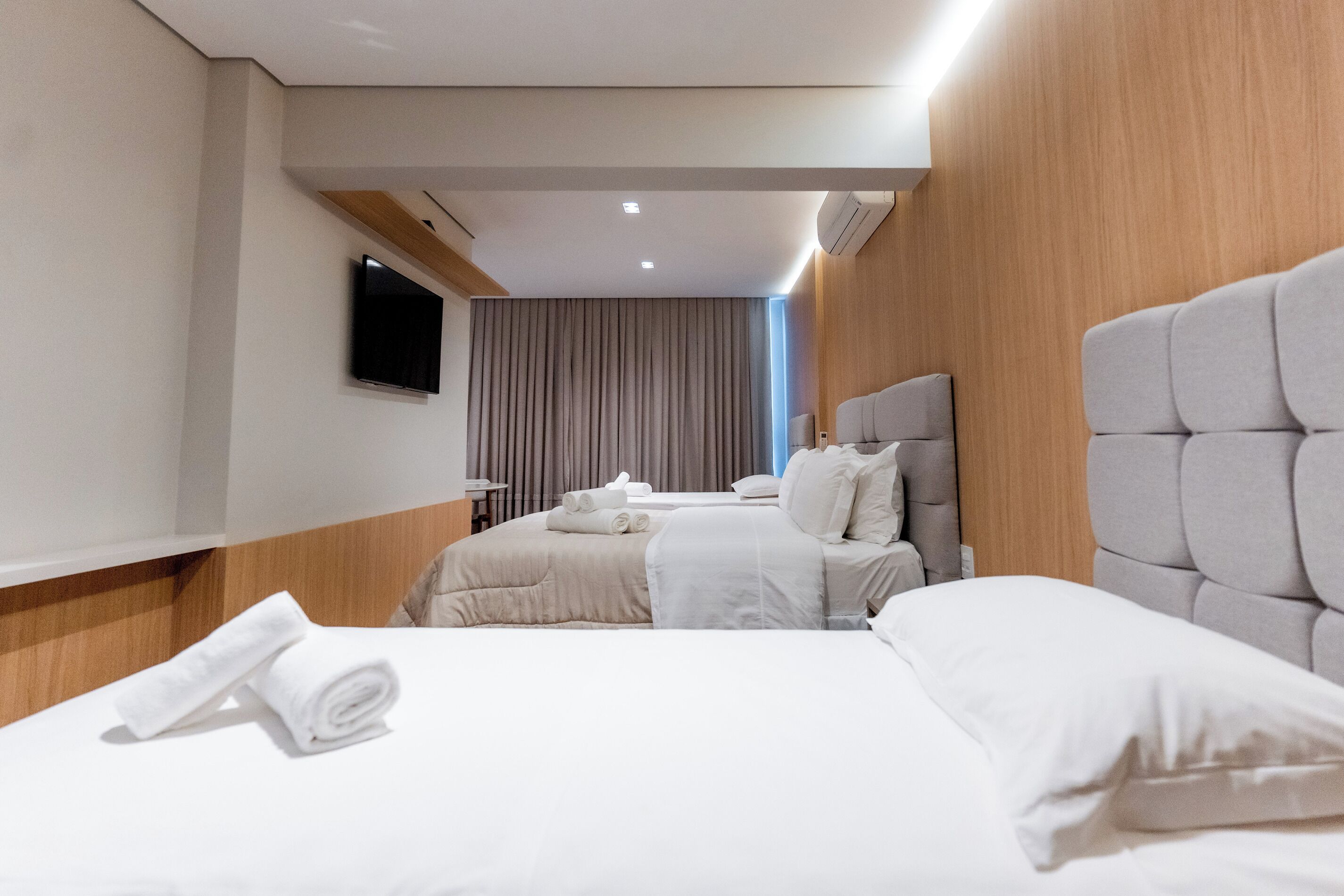 A hotel room with two beds, a flat-screen TV mounted on the wall, and a wooden panel design on the walls.