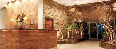 Una zona de recepción con mostrador de madera, pared de piedra y plantas de interior.