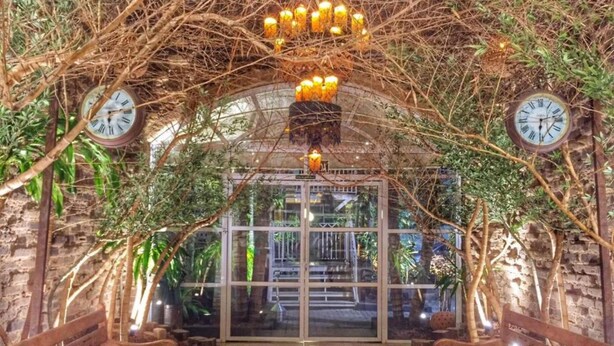 An indoor garden with wooden benches, a glass door entrance, and clocks on the walls. - Beira Rio Palace Hotel (Piracicaba)