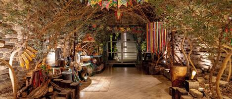 An indoor setting with a wooden floor, stone walls, and a central aisle leading to a large, illuminated structure.