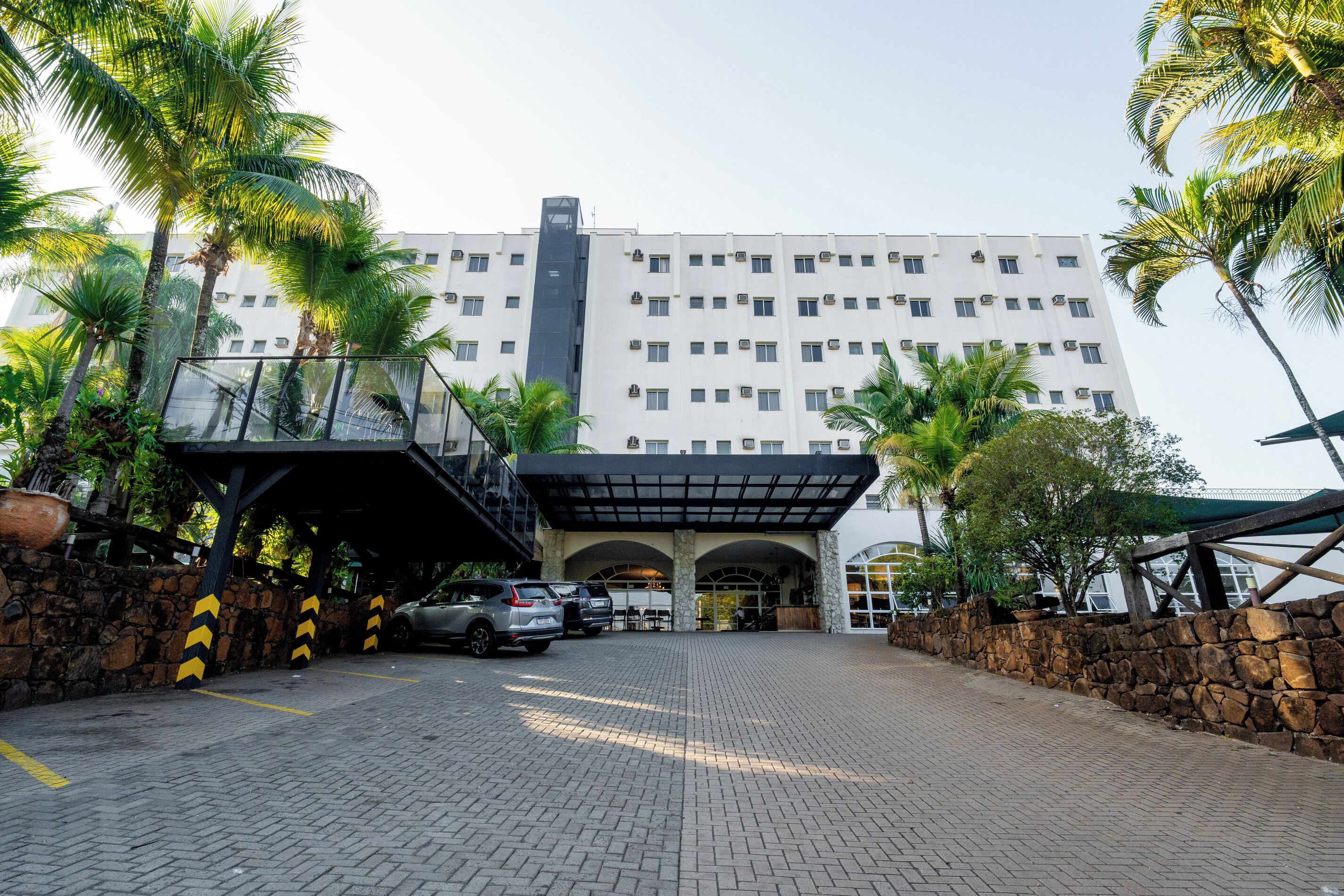 A hotel entrance with a covered parking area, stone walls, and palm trees.