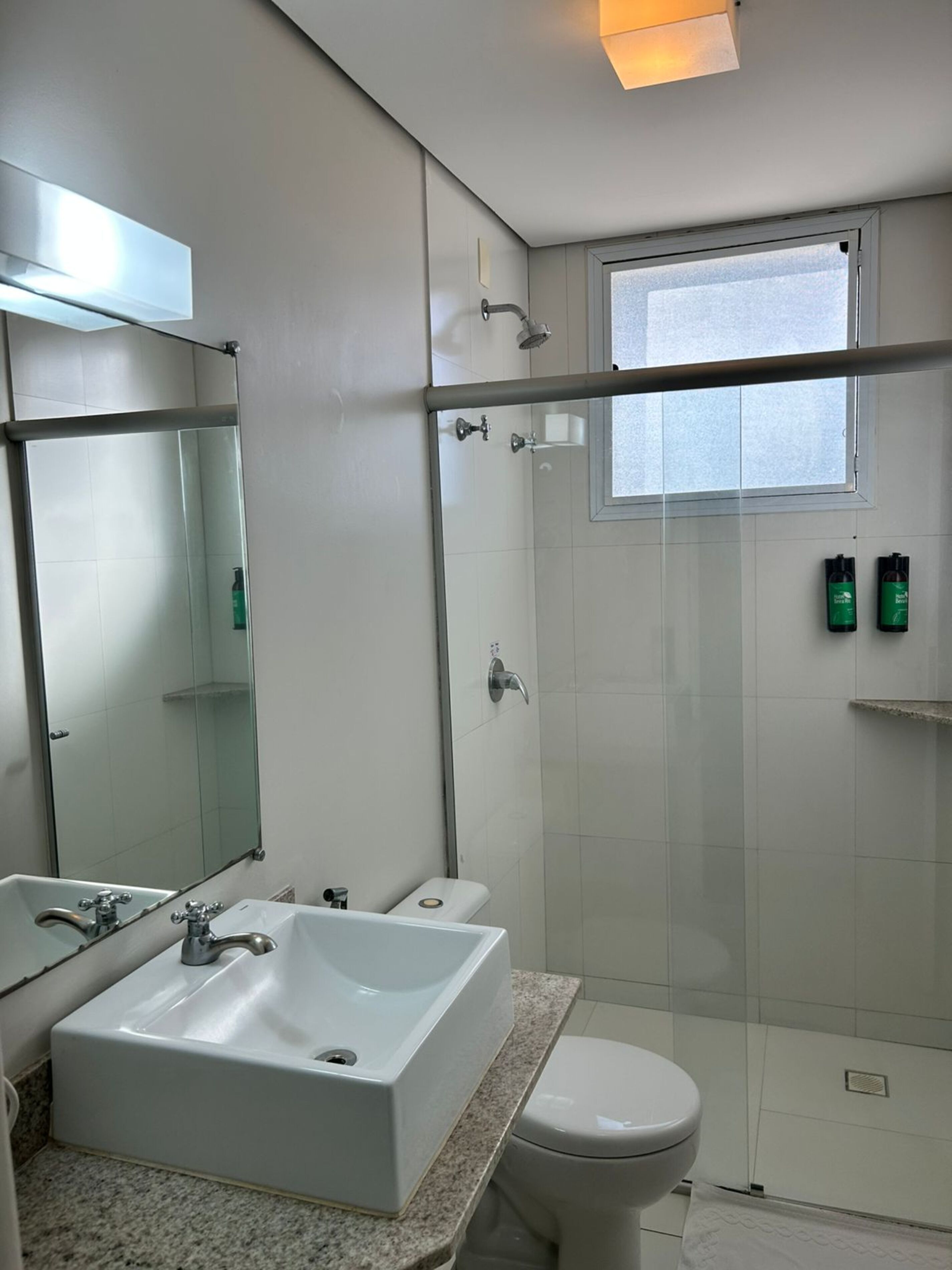 A modern bathroom with a large sink, a toilet, a glass shower enclosure, and a window.