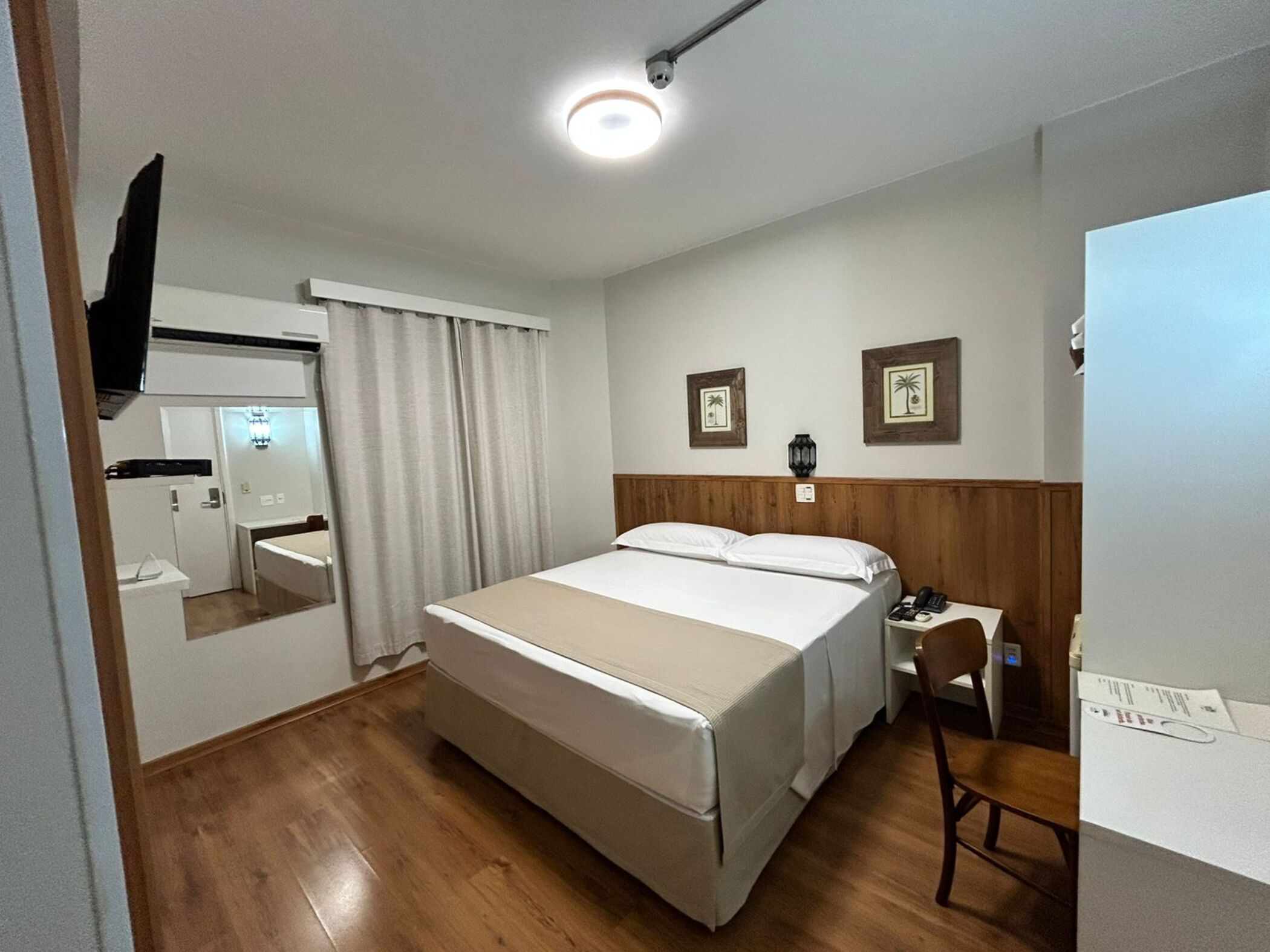 Habitación de hotel con cama, escritorio, silla, espejo y baño con lavamanos e inodoro.