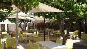 An outdoor patio with yellow chairs and tables, covered by umbrellas, surrounded by trees. - Hotel Los Bartolos (Alhama de Murcia)