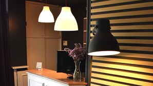 A reception desk with a white counter, two pendant lights, a black floor lamp, and a vase with purple flowers. - Hotel Los Bartolos (Alhama de Murcia)